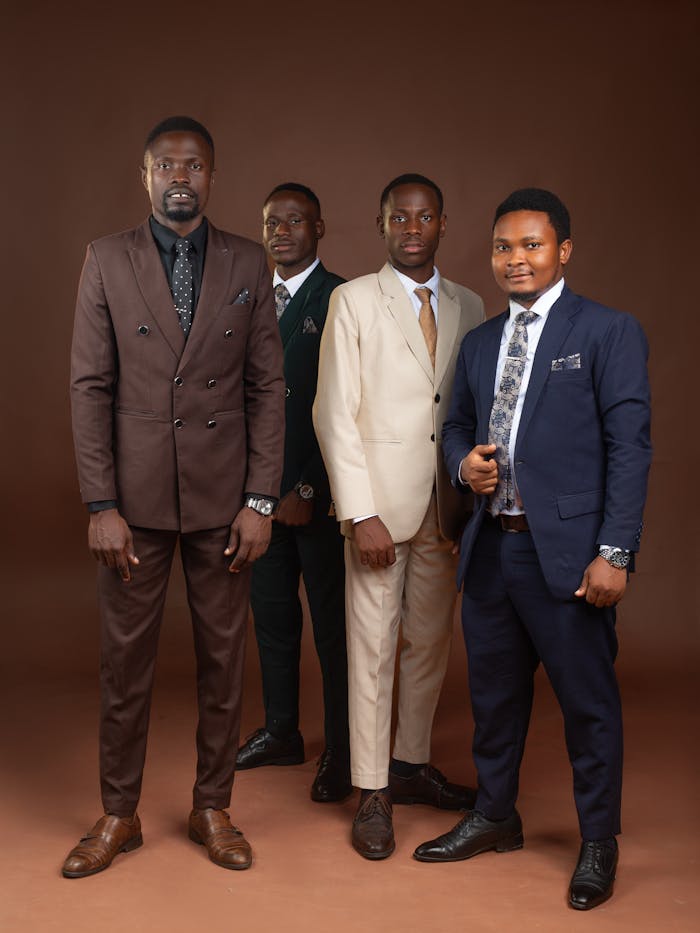 Four men in formal suits posing confidently in a studio setting.