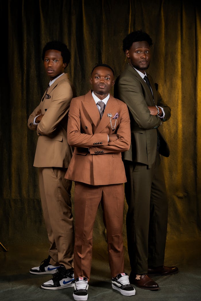 Three men in fashionable suits posing confidently against a dark backdrop.